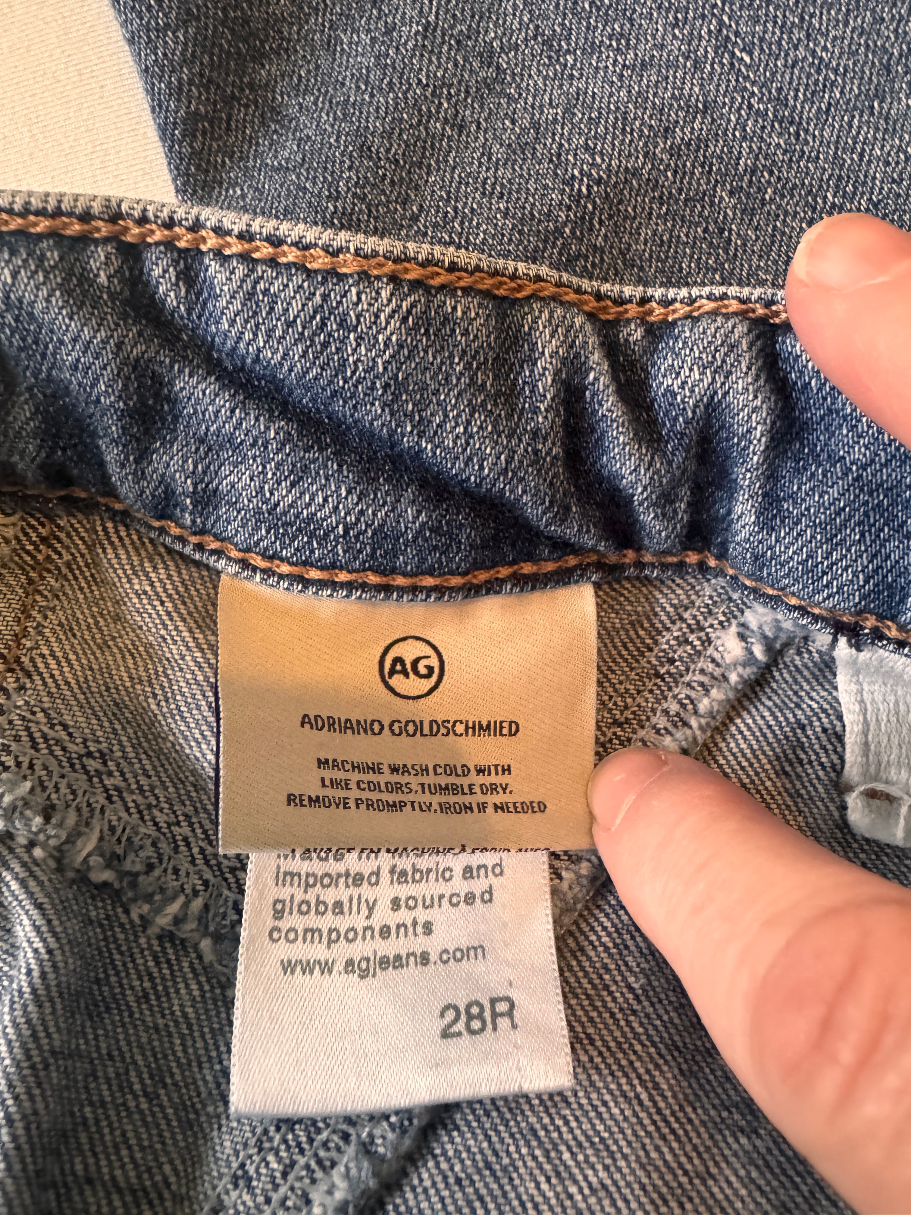 Close-up of a denim fabric with a brand label held by a hand.