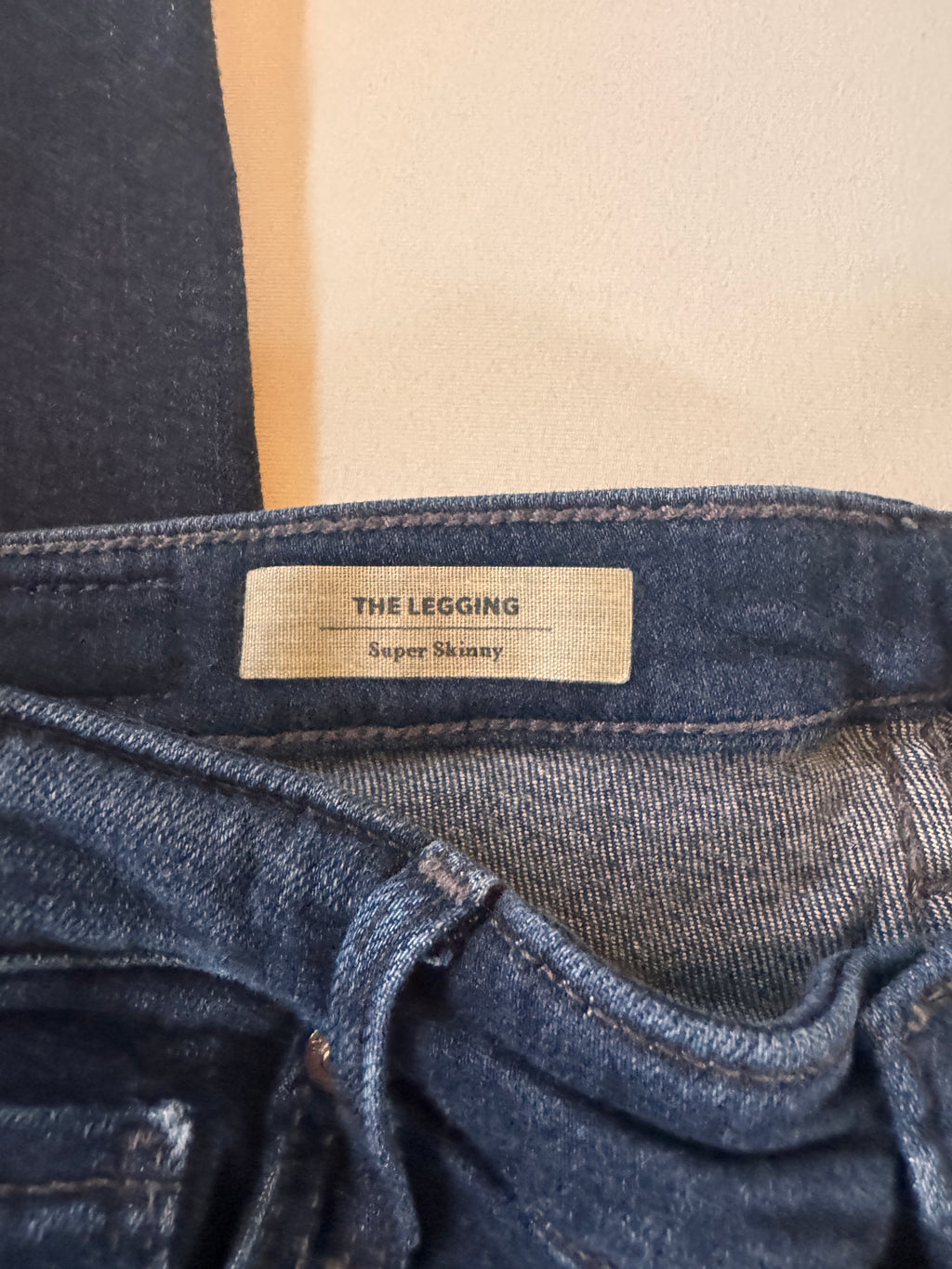 Close-up of a denim legging with a brand label on a beige background