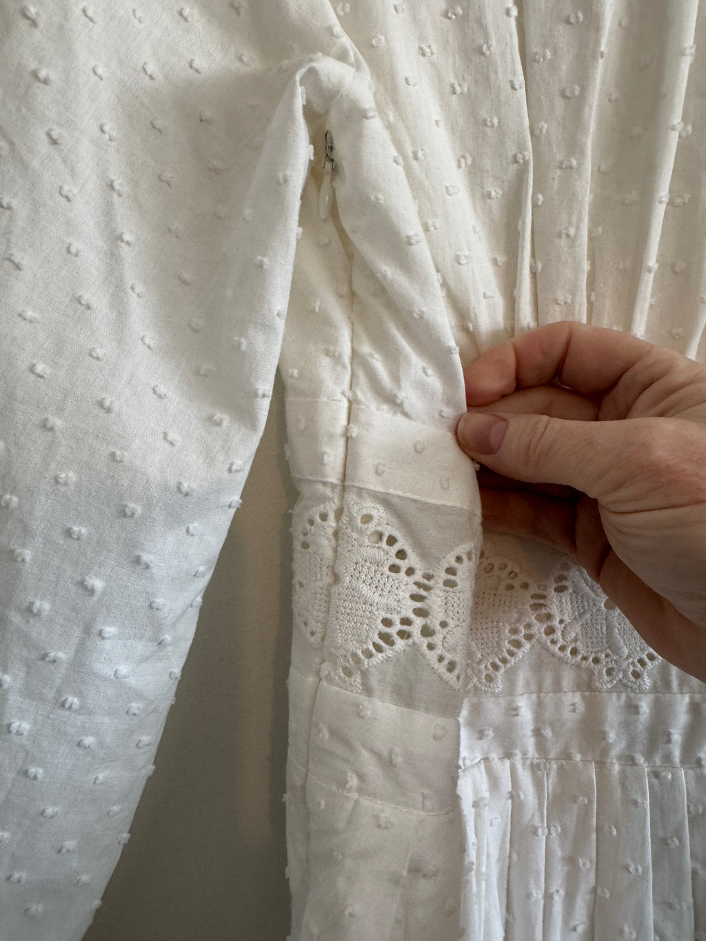 Close-up of a hand holding white fabric with intricate lace detailing.