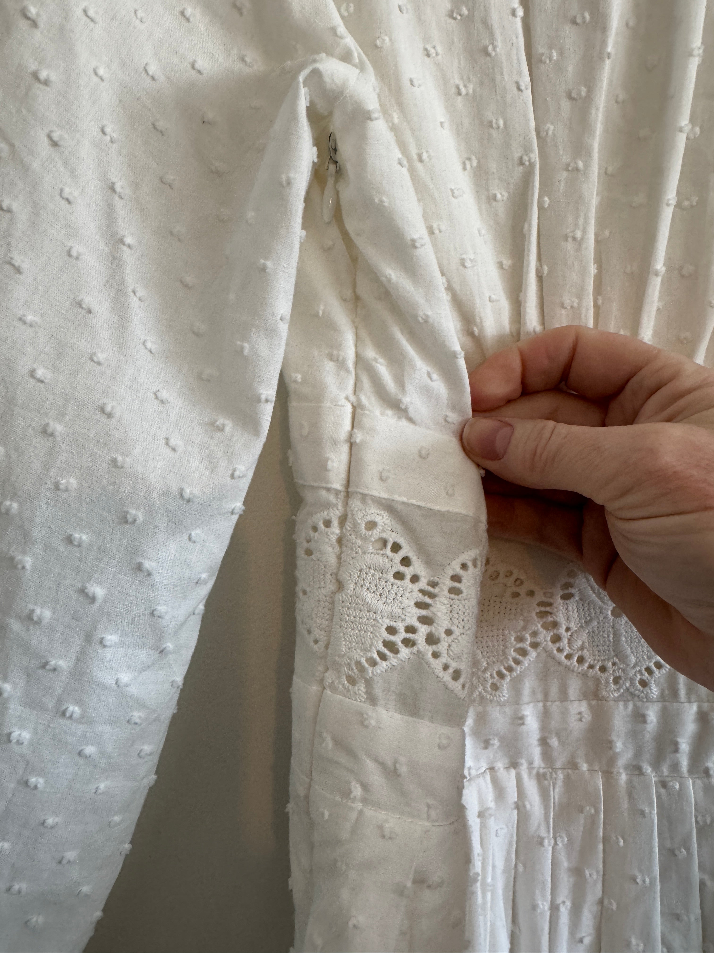 Close-up of a hand holding white fabric with intricate lace detailing.