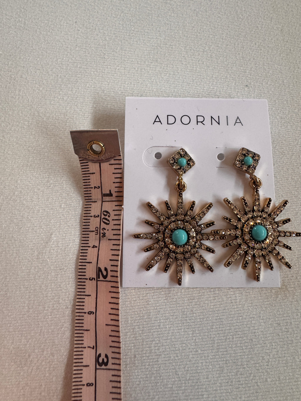 Sun-shaped earrings with turquoise stones on an Adornia card, measured against a ruler.