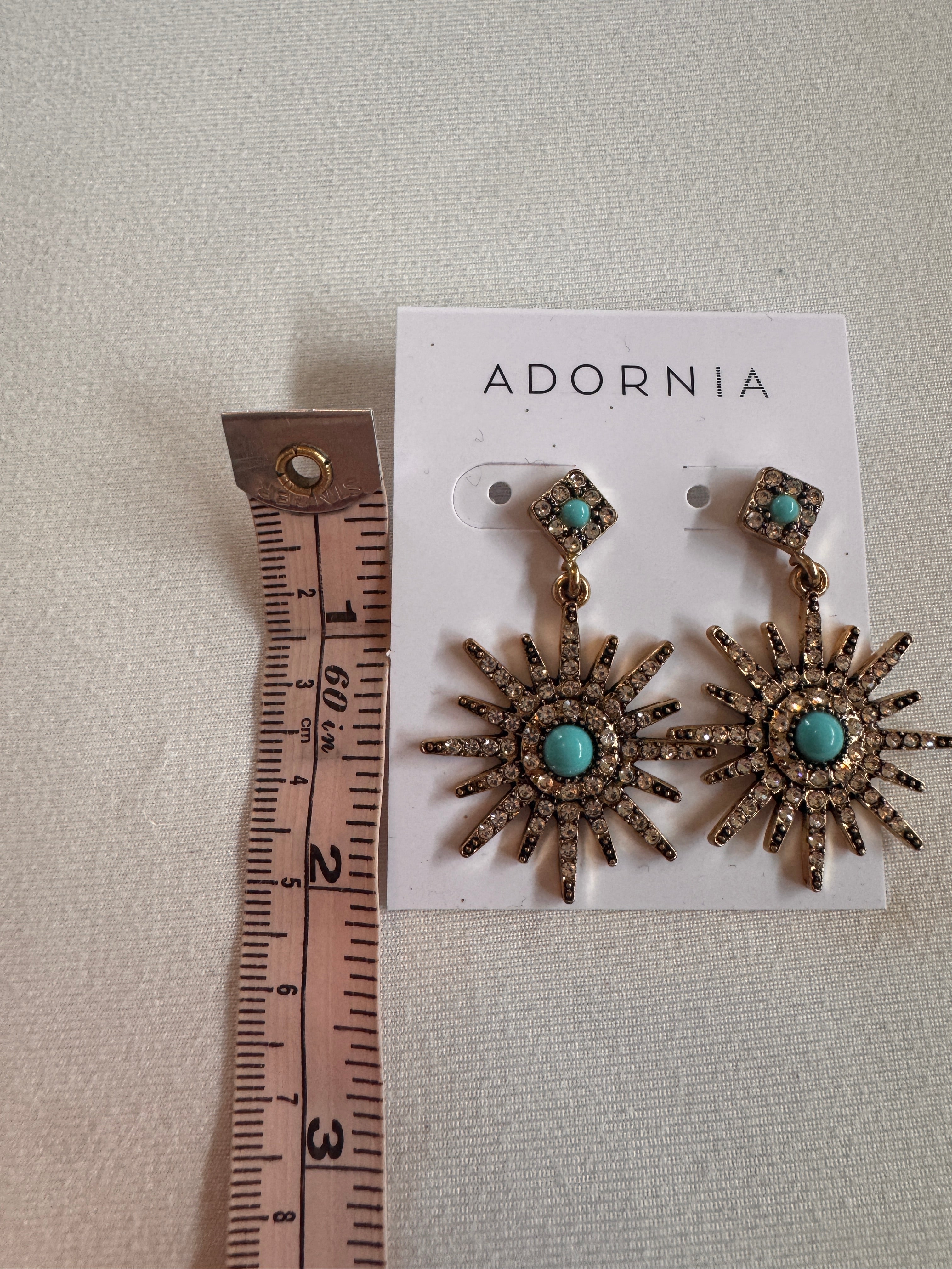 Sun-shaped earrings with turquoise stones on an Adornia card, measured against a ruler.