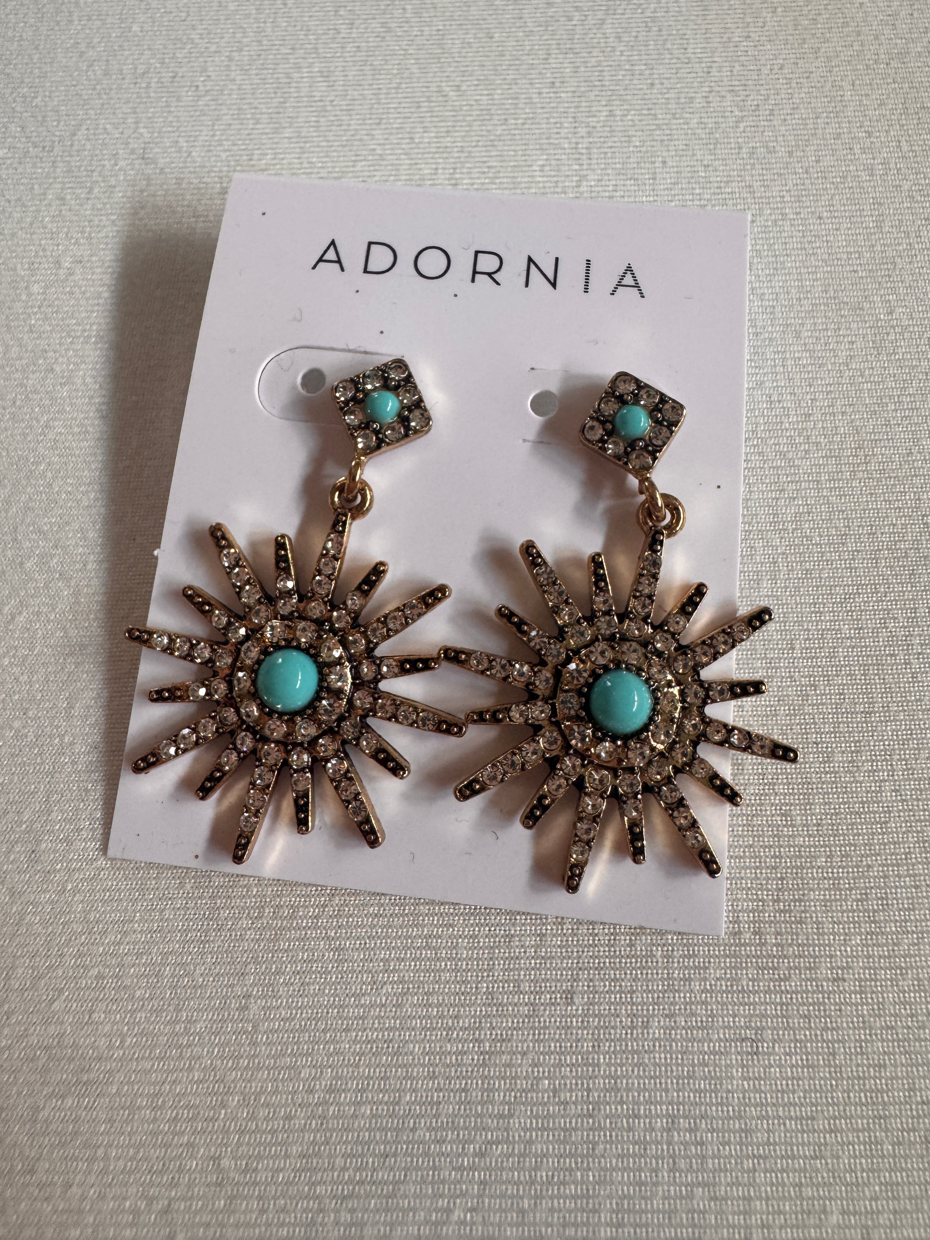 Pair of sunflower-shaped earrings with turquoise stones on a branded card against a textured gray background.