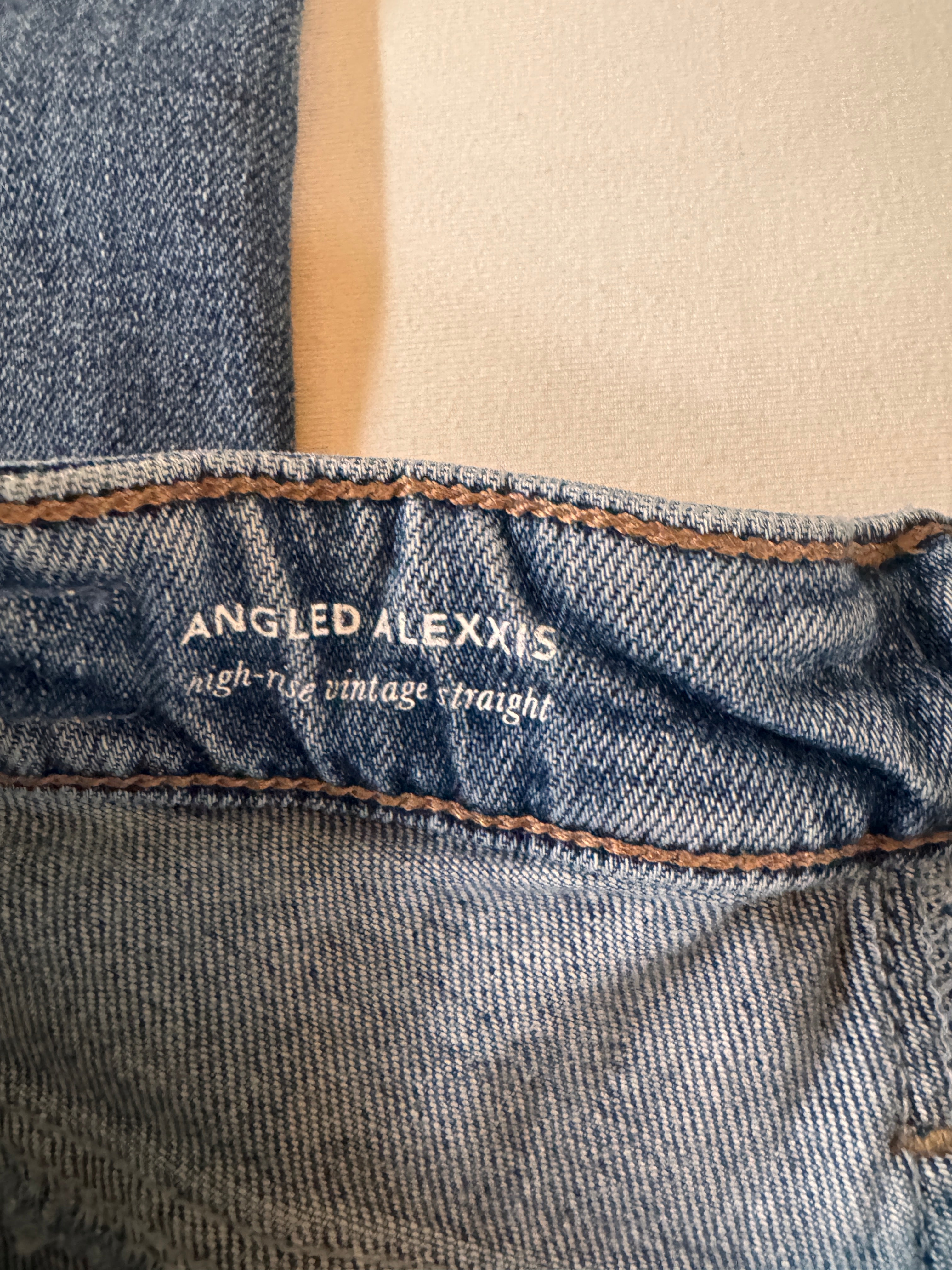 Close-up of blue jeans with 'Angled Alexxis' branding on a beige background