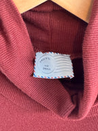 Close-up of a rust knit top with a small white label featuring blue text and red dots.