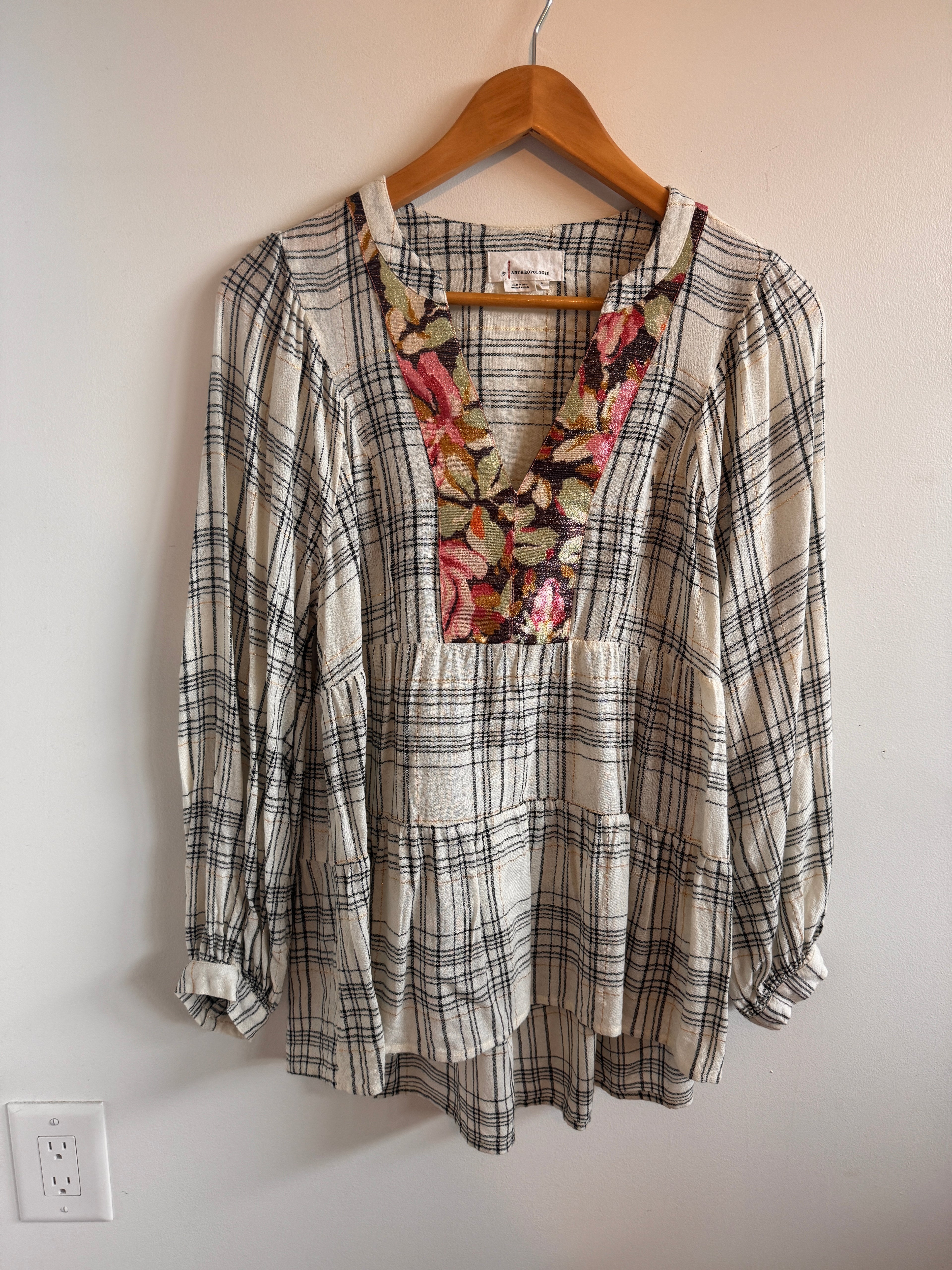 Plaid shirt with floral patch on a hanger against a plain wall.