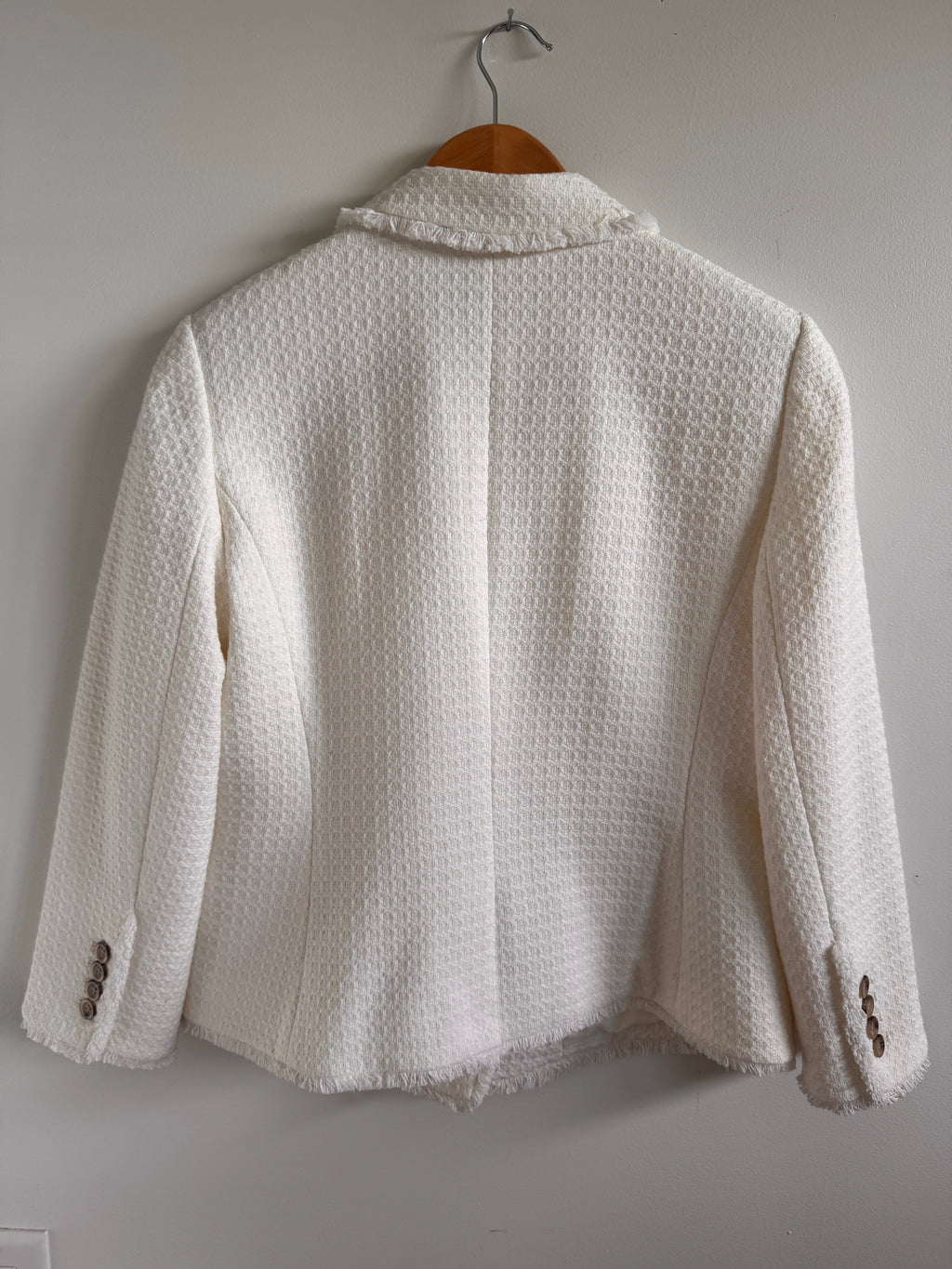 White textured jacket on a hanger against a light gray background