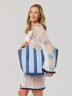 Woman holding a blue and white striped beach bag against a plain background