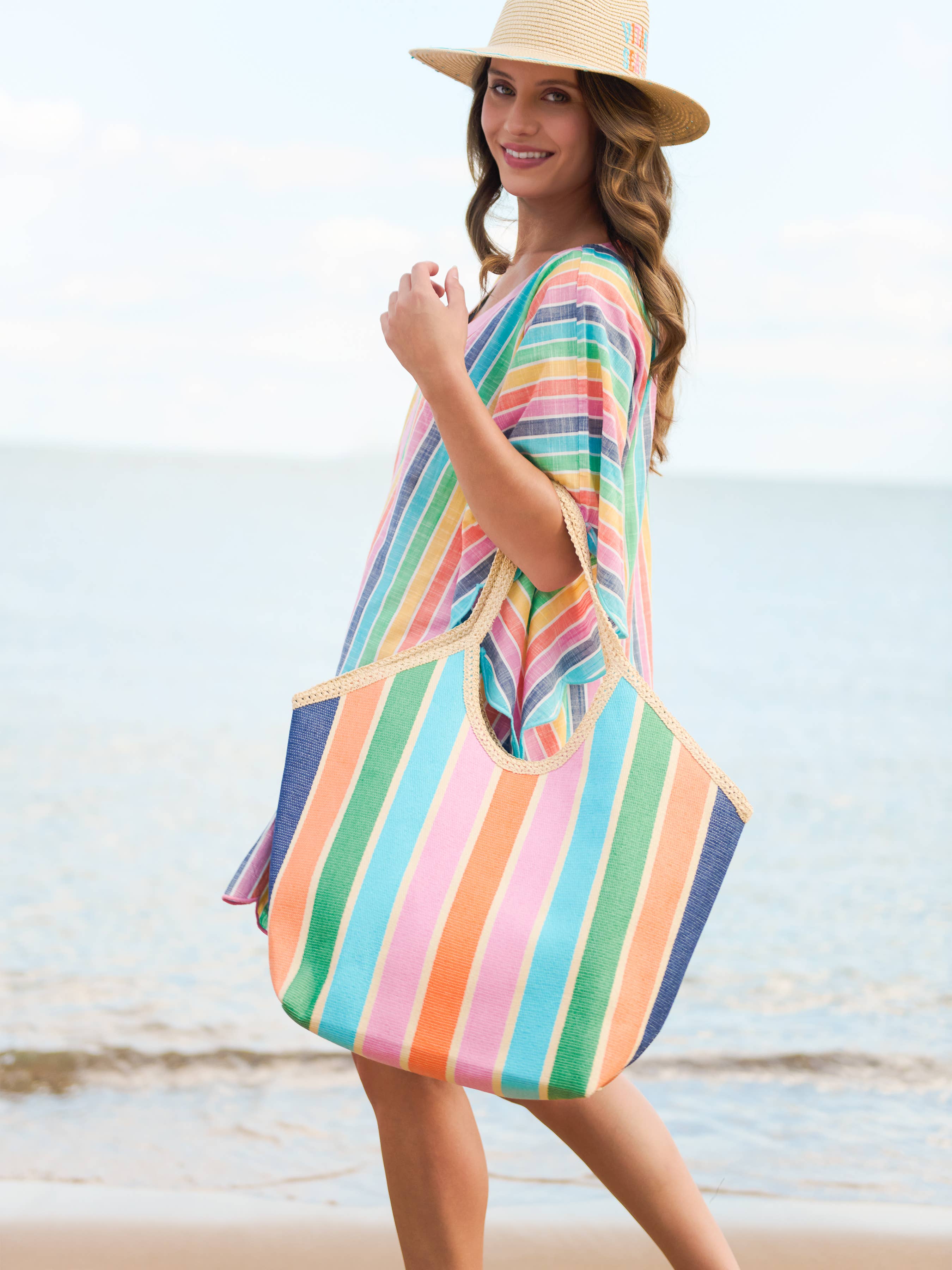 Woman in a colorful striped dress and hat standing on a beach.