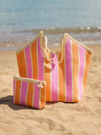 Striped beach bag and pouch on a sandy beach with ocean in the background