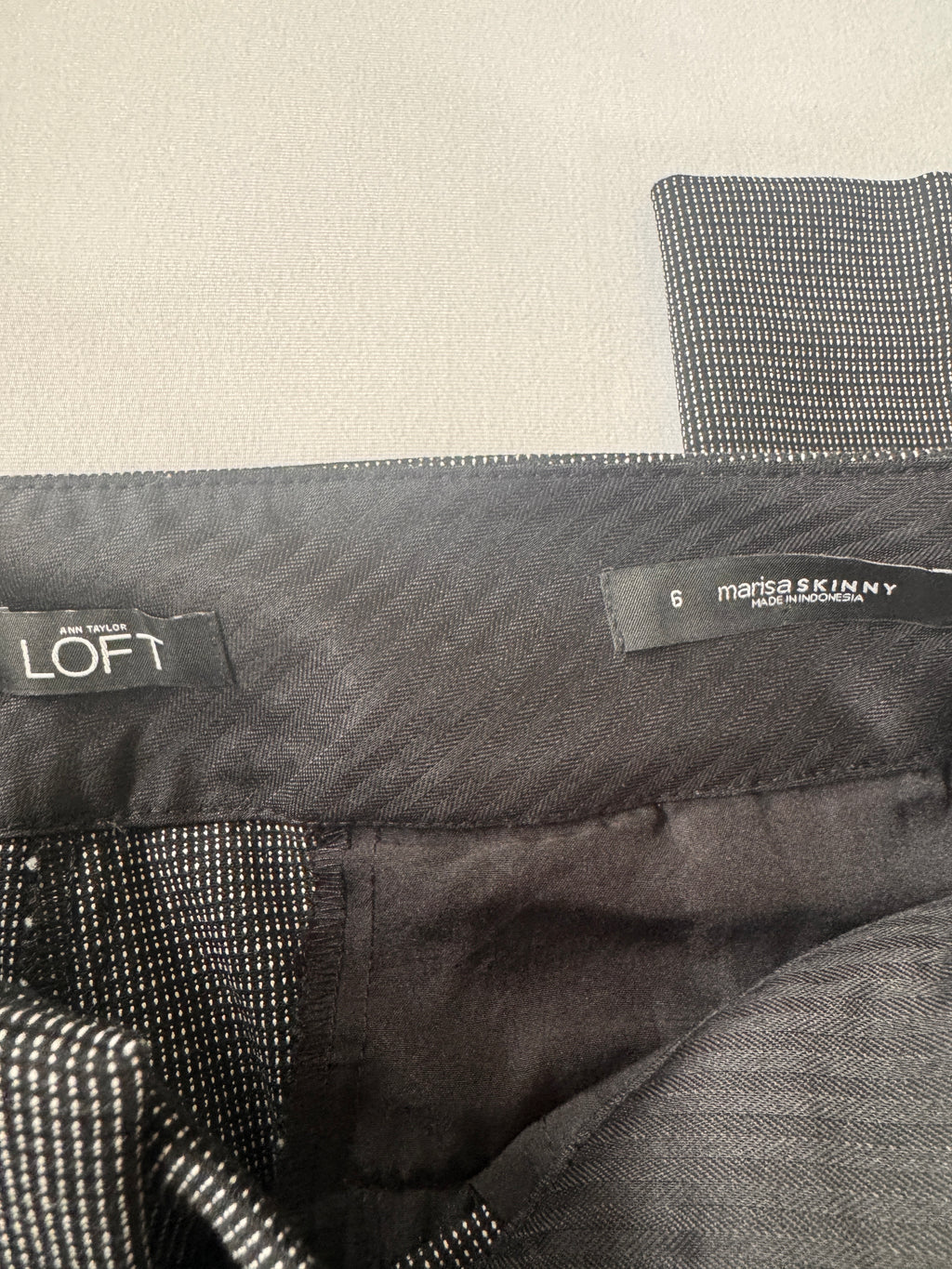 Close-up of a gray jacket with 'LOFT' and 'Marisa Skinny' labels on a beige background