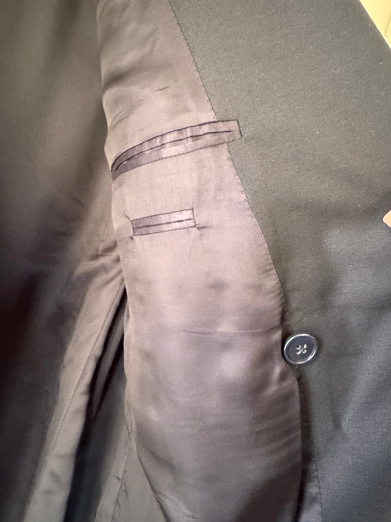 Close-up detail of a navy-colored suit jacket, showing the interior lining, a button closure, and a welt pocket.