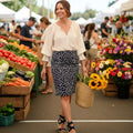 Woman shopping at an outdoor farmers market with produce and flowers around her.