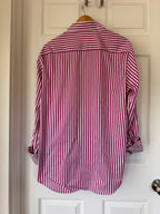 A long-sleeve button-up shirt with vertical red and white stripes, hanging on a wooden hanger against a white paneled door.