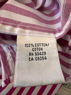 Close-up of a garment's interior neck label reading '100% COTTON' with pink and white striped fabric visible around it.