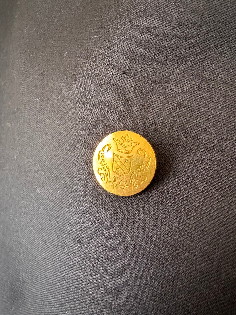 A small round gold button with an embossed lion design, placed on a dark gray textured fabric background.