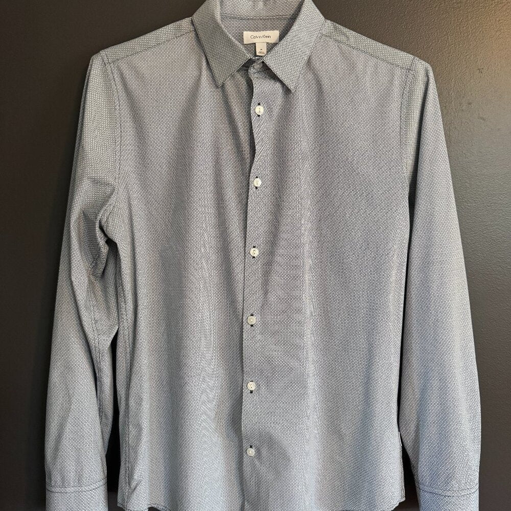 Gray patterned shirt on a hanger against a dark background