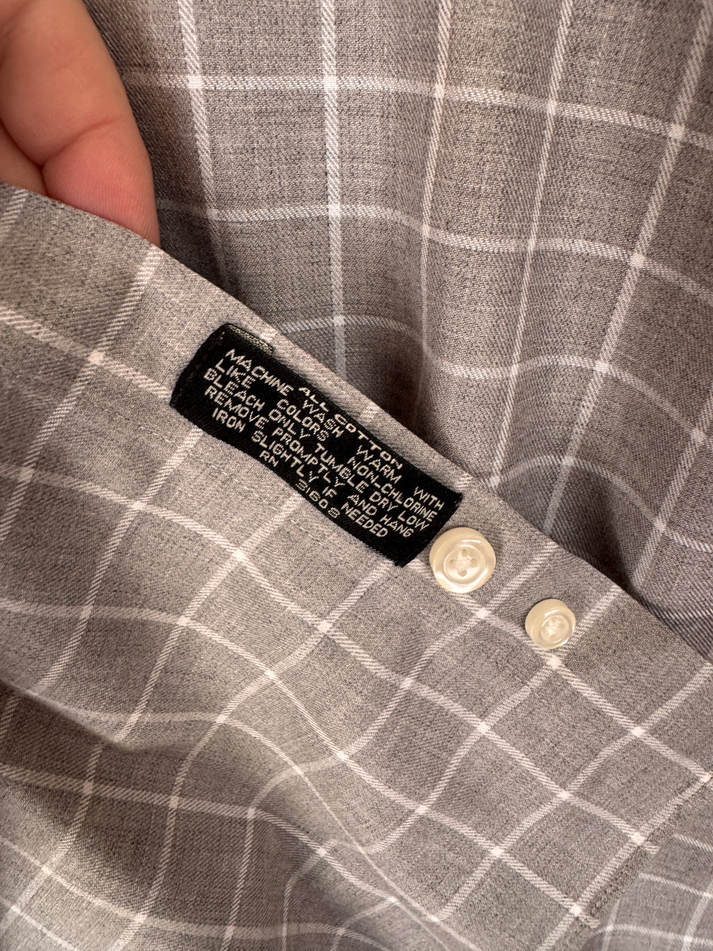 Close-up of a gray and white plaid shirt showing the inner collar label and two cream-colored buttons.