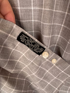 Close-up of a gray and white plaid shirt showing the inner collar label and two cream-colored buttons.