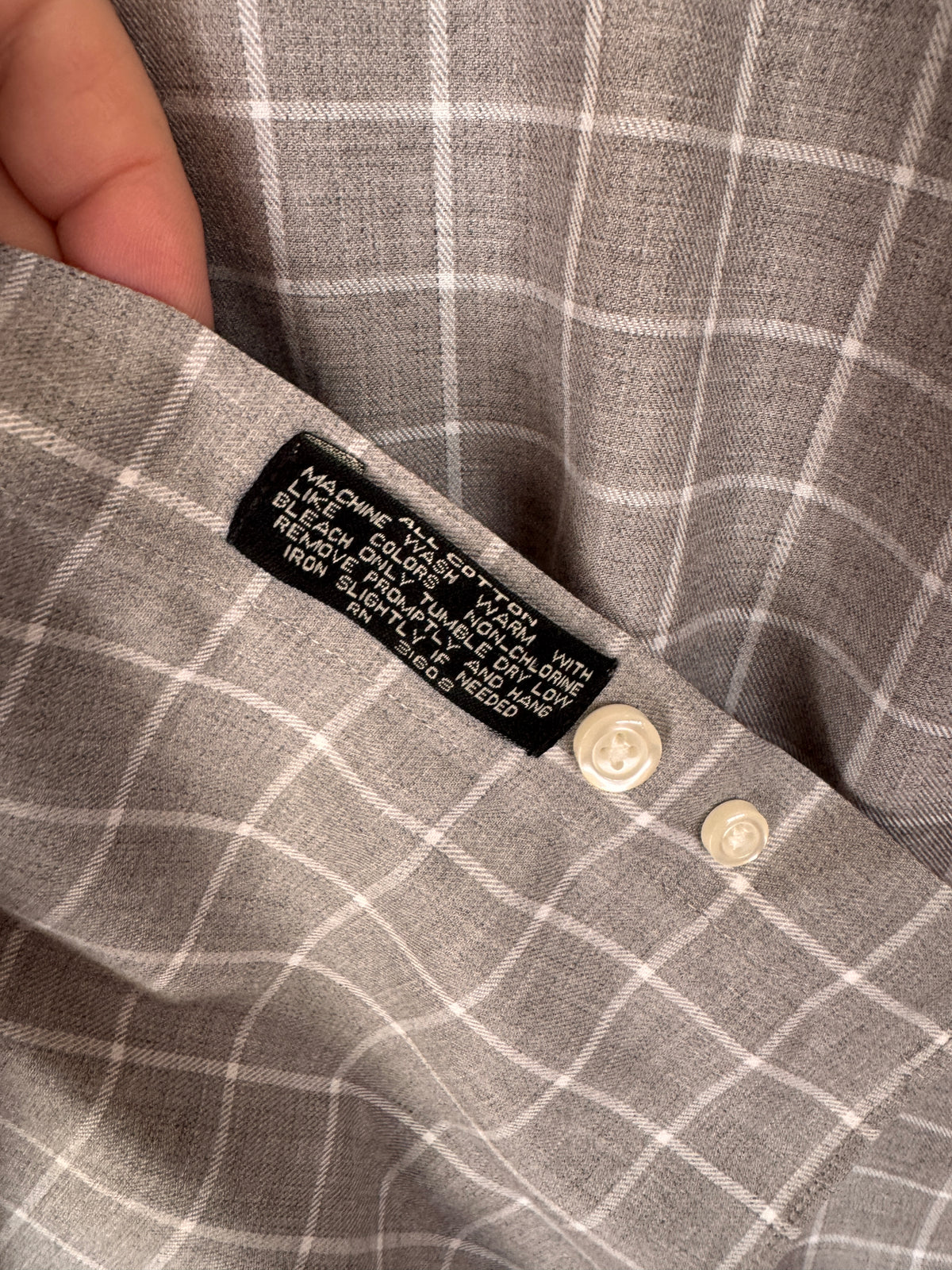 Close-up of a gray and white plaid shirt showing the inner collar label and two cream-colored buttons.