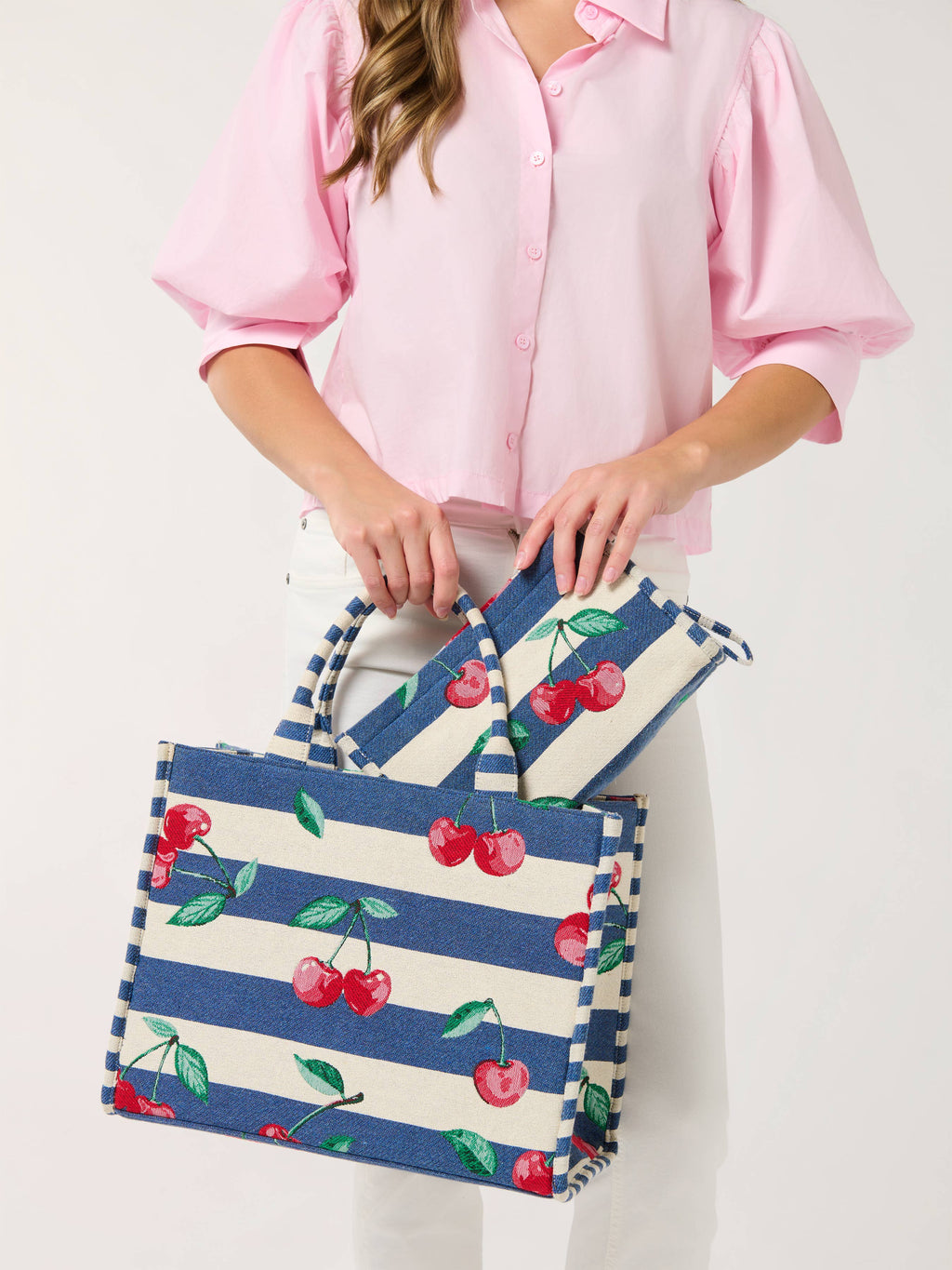 Person holding a striped tote bag with cherry design against a white background