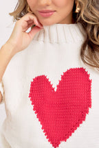 White sweater with a large red heart design worn by a person.