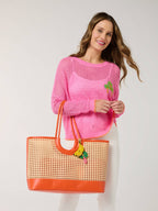 Woman wearing a pink sweater holding a straw bag with orange trim on a white background