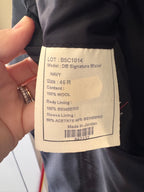 A close-up of a garment's interior label showing details for the 'DB Signature Blazer' in navy wool, held by a hand with a ring.