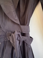 Close-up of a black fabric garment with gathered pleats and a tie detail, photographed against a light wall.