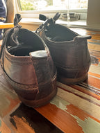 Pair of brown shoes leaning against a wooden wall.