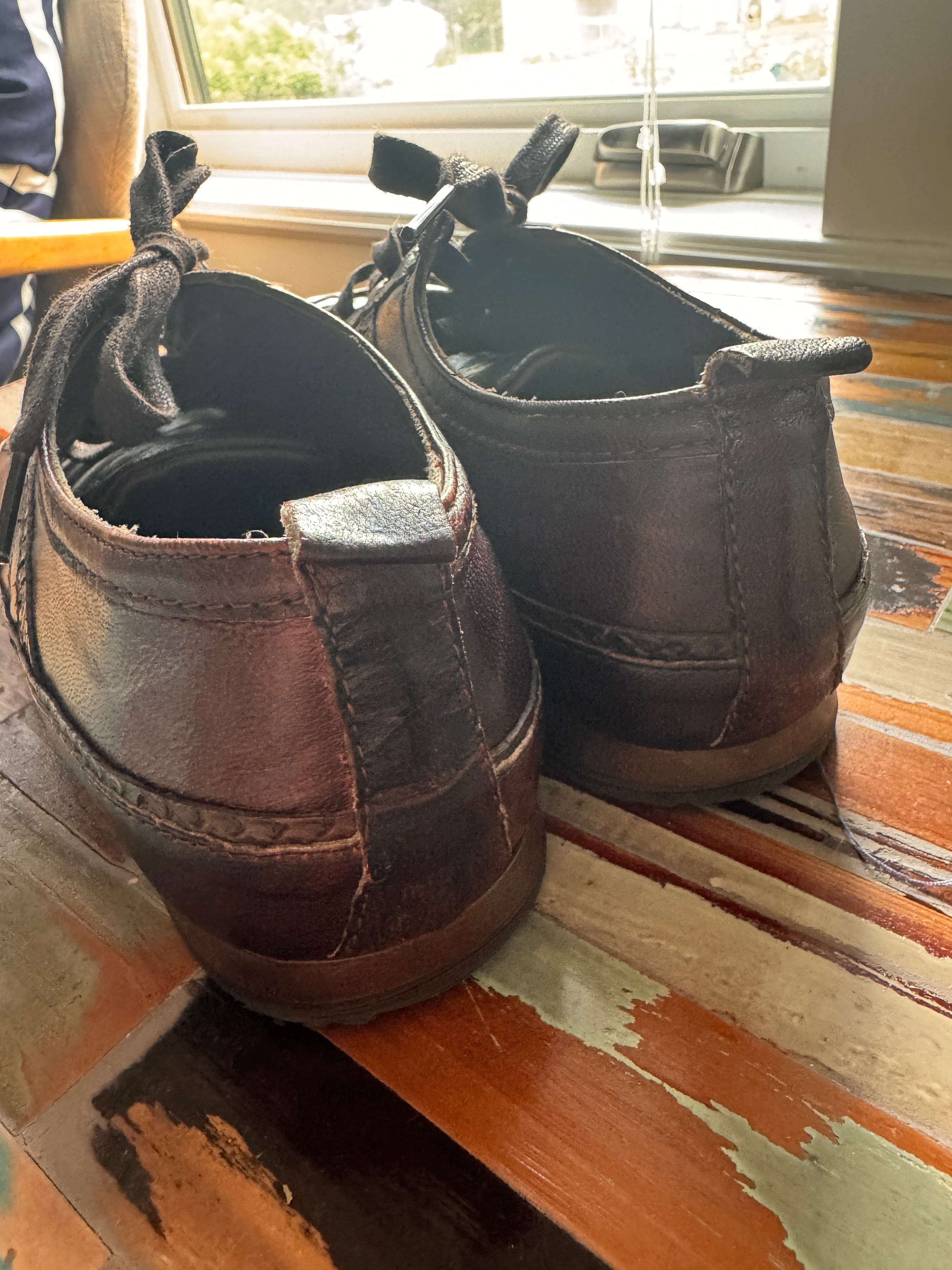 Pair of brown shoes leaning against a wooden wall.