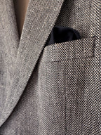 Close-up of a textured herringbone tweed blazer in gray and beige, with a black pocket square tucked into the chest pocket.