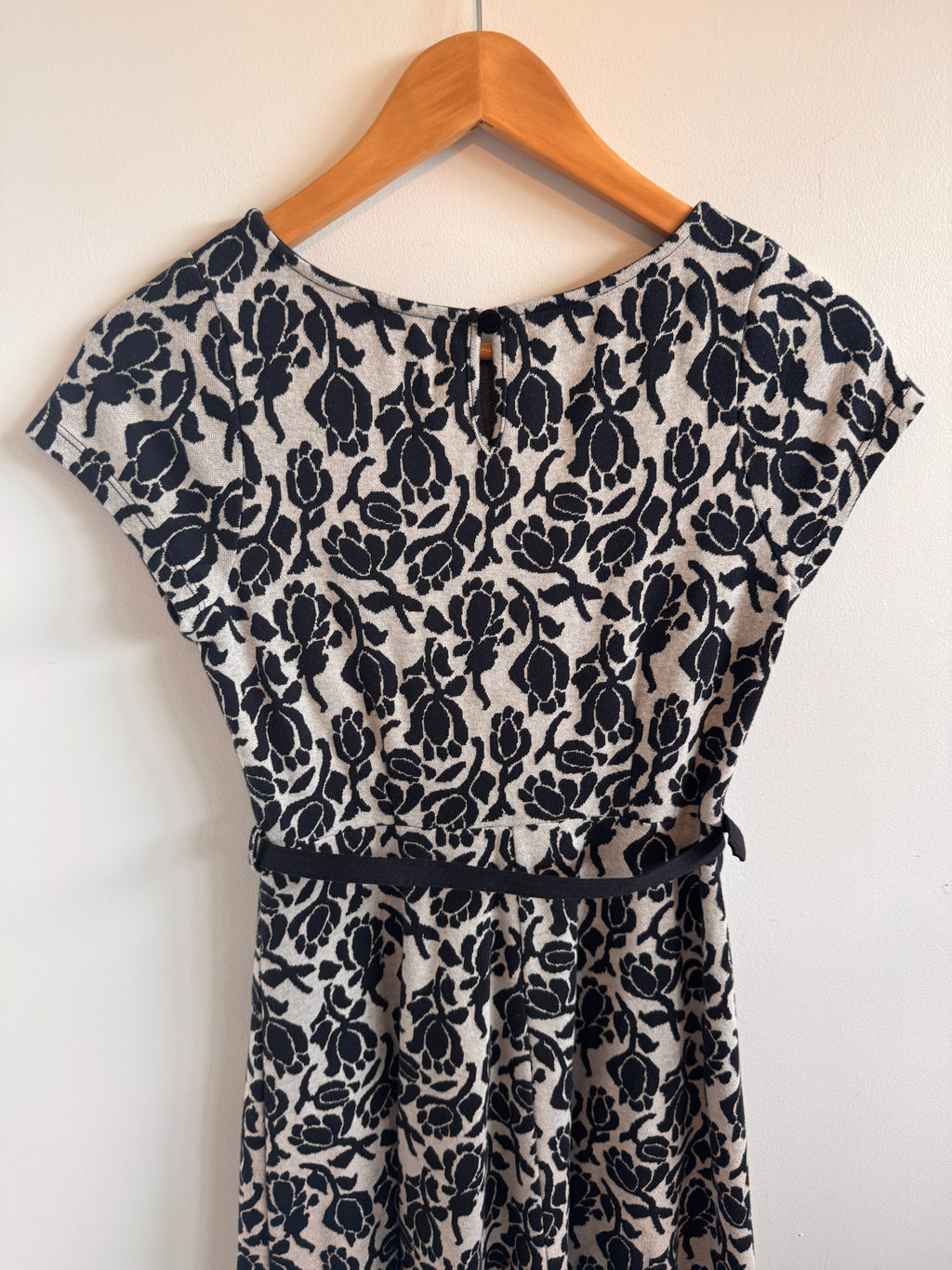 Black floral-patterned dress on a wooden hanger against a white background