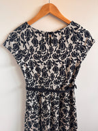 Black floral-patterned dress on a wooden hanger against a white background