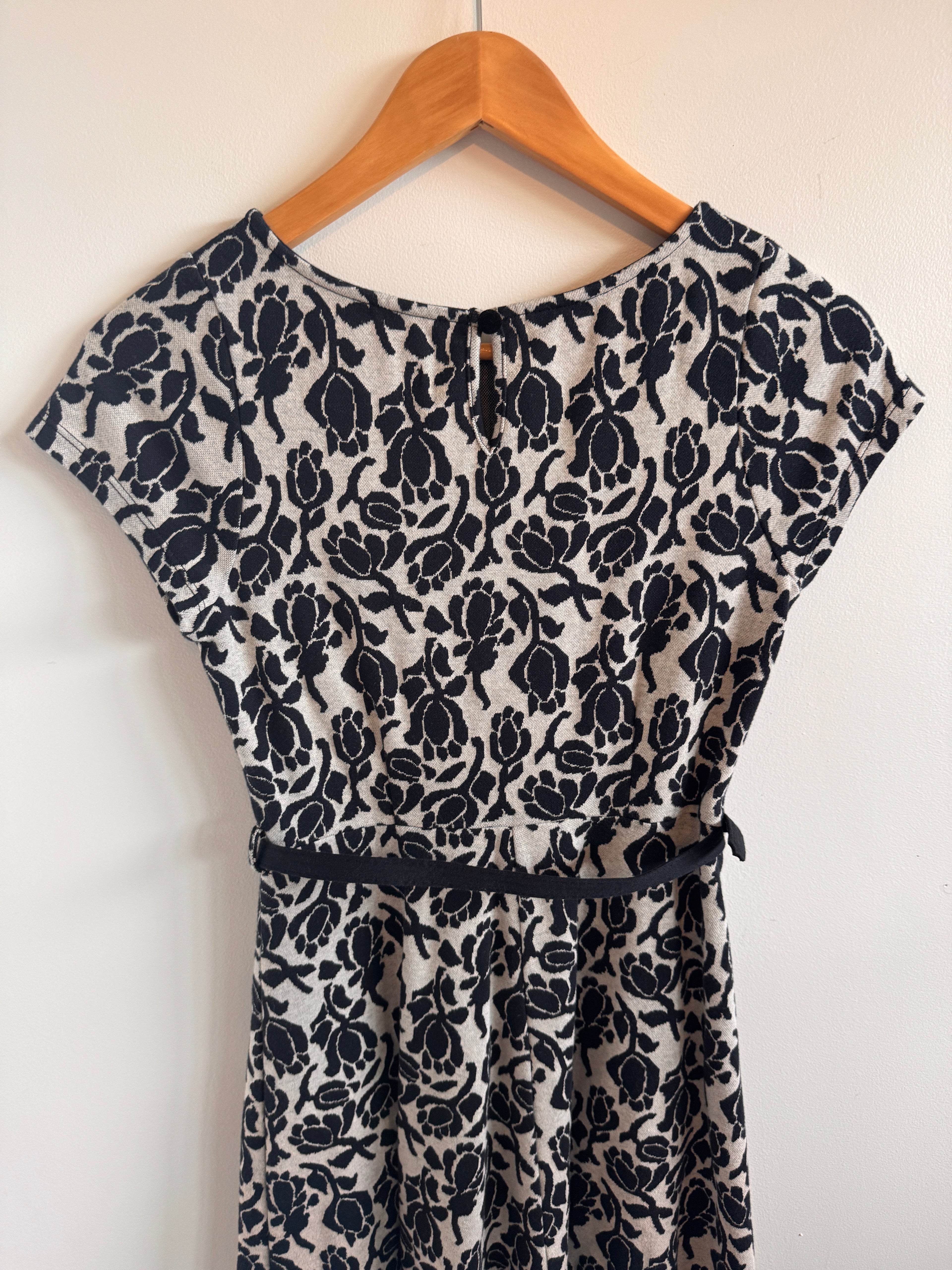 Black floral-patterned dress on a wooden hanger against a white background