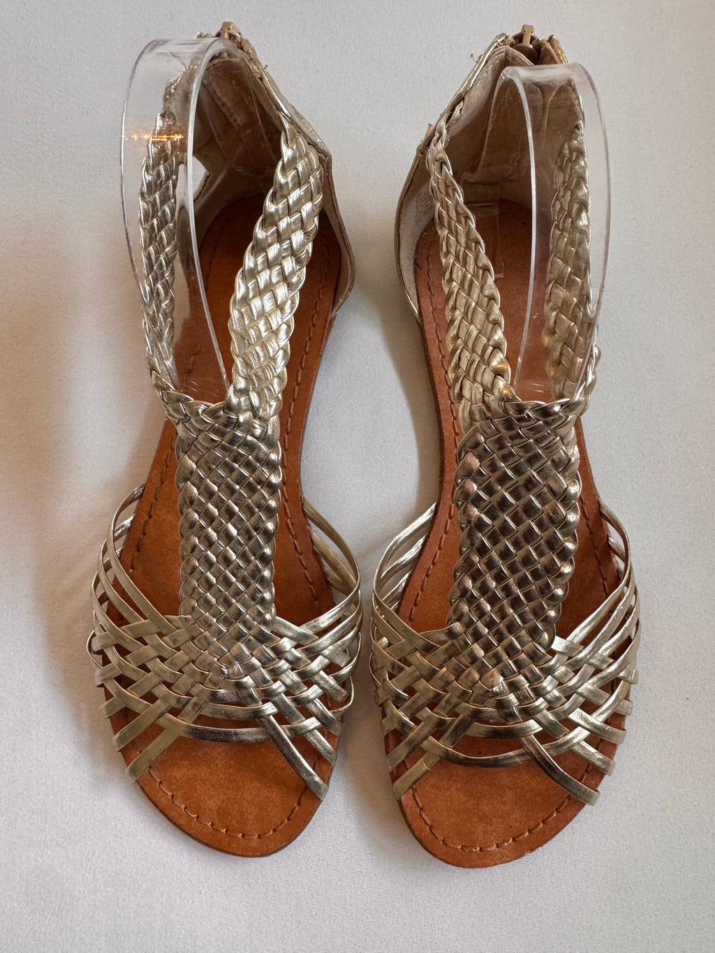 Pair of gold woven sandals on a white background
