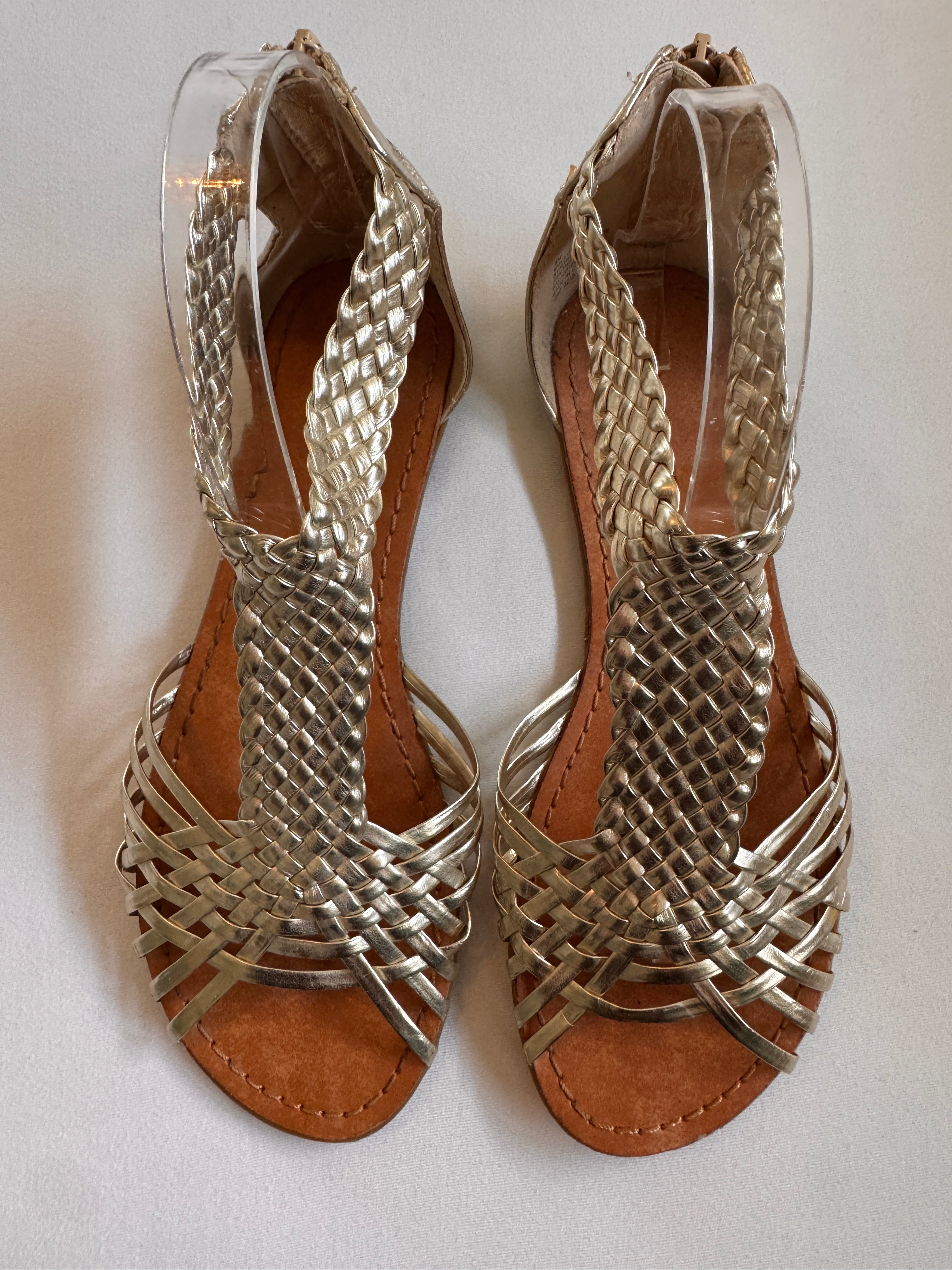 Pair of gold woven sandals on a white background