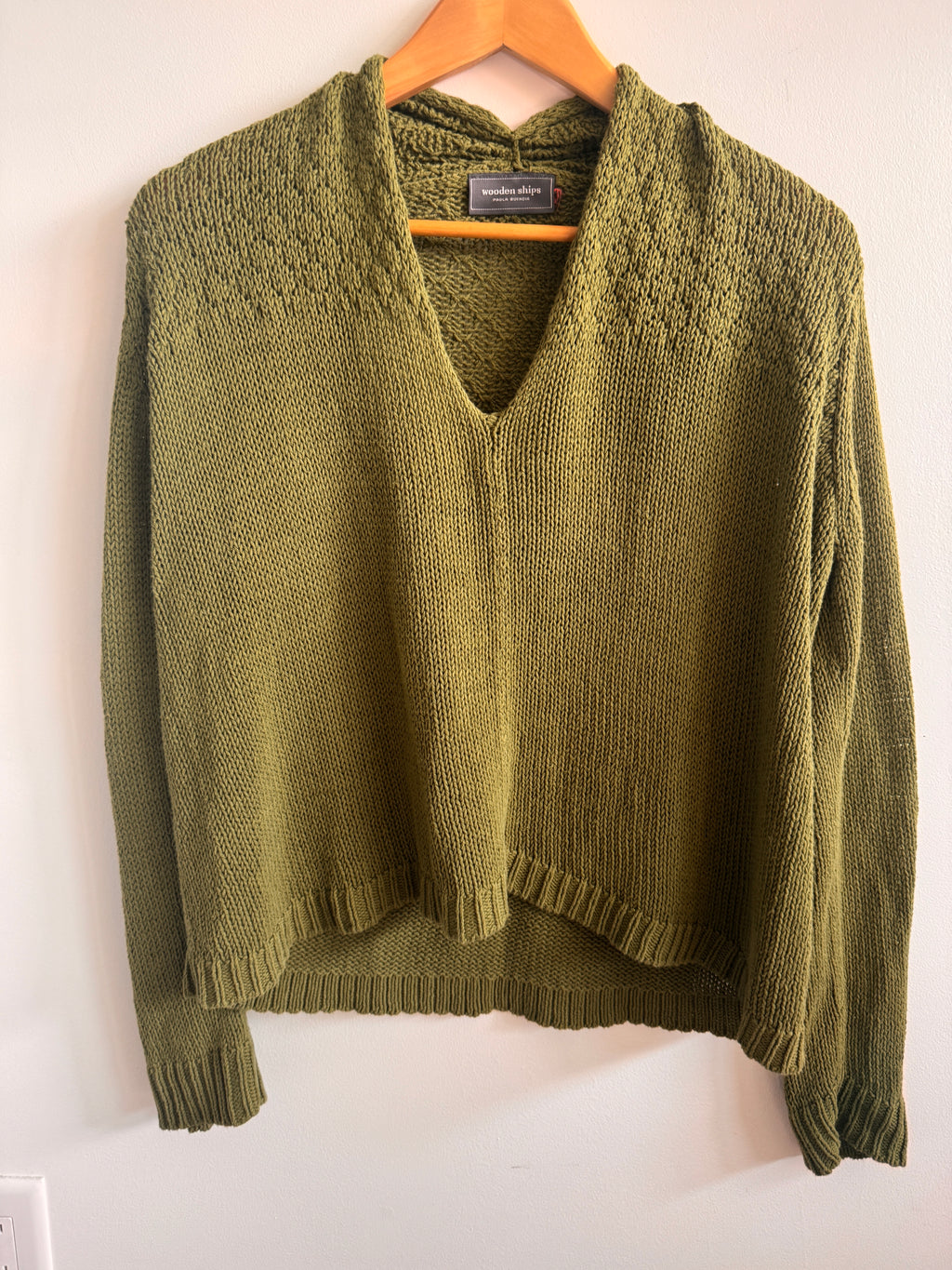Green knitted sweater on a wooden hanger against a white background