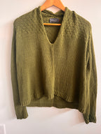 Green knitted sweater on a wooden hanger against a white background