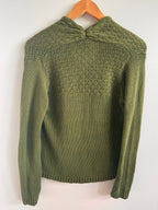 Green knitted sweater on a wooden hanger against a white background