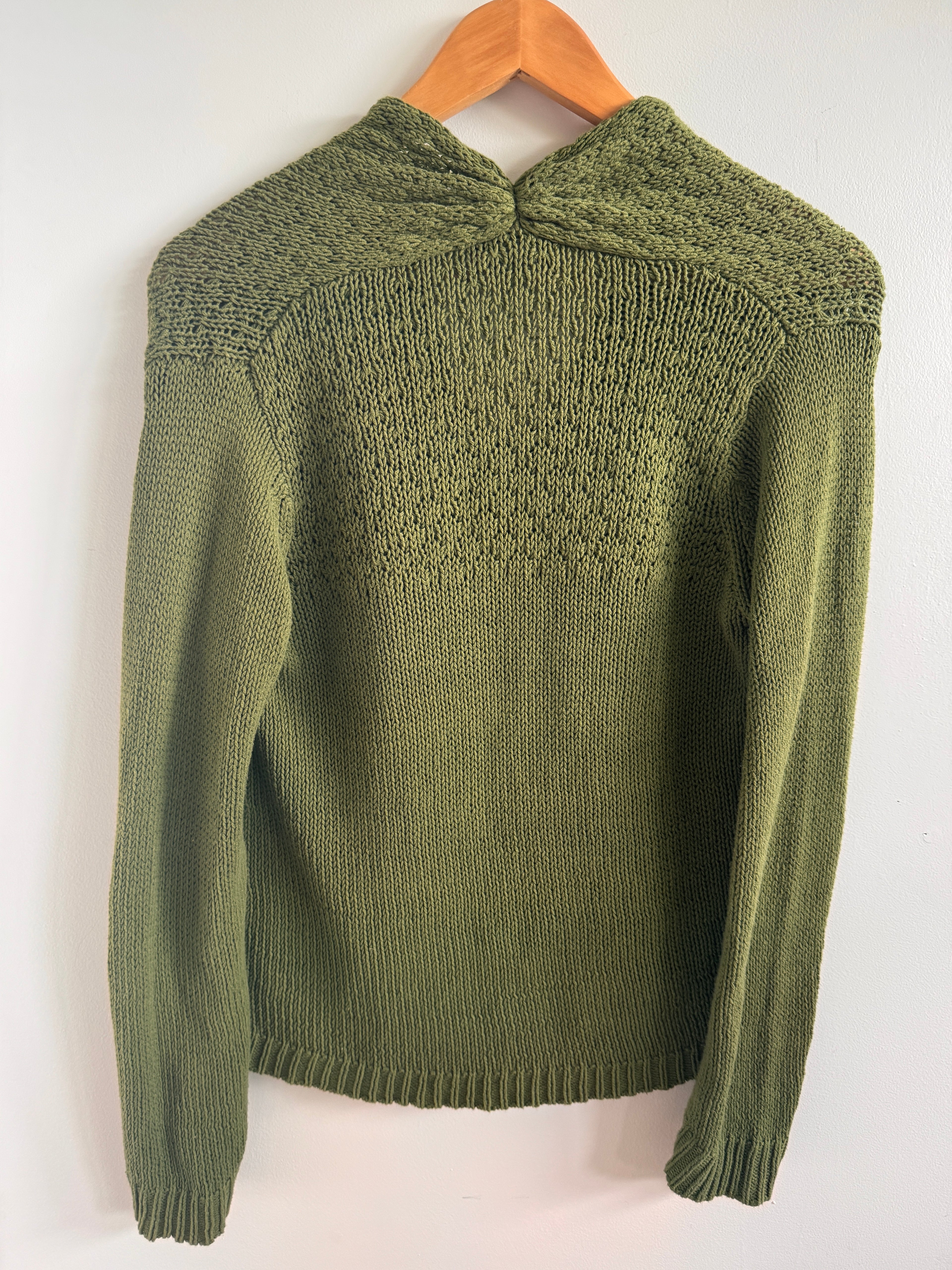 Green knitted sweater on a wooden hanger against a white background