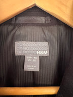 Close-up of the interior neck label of a black H&M garment hanging on a wooden hanger, showing the H&M brand name and size information.