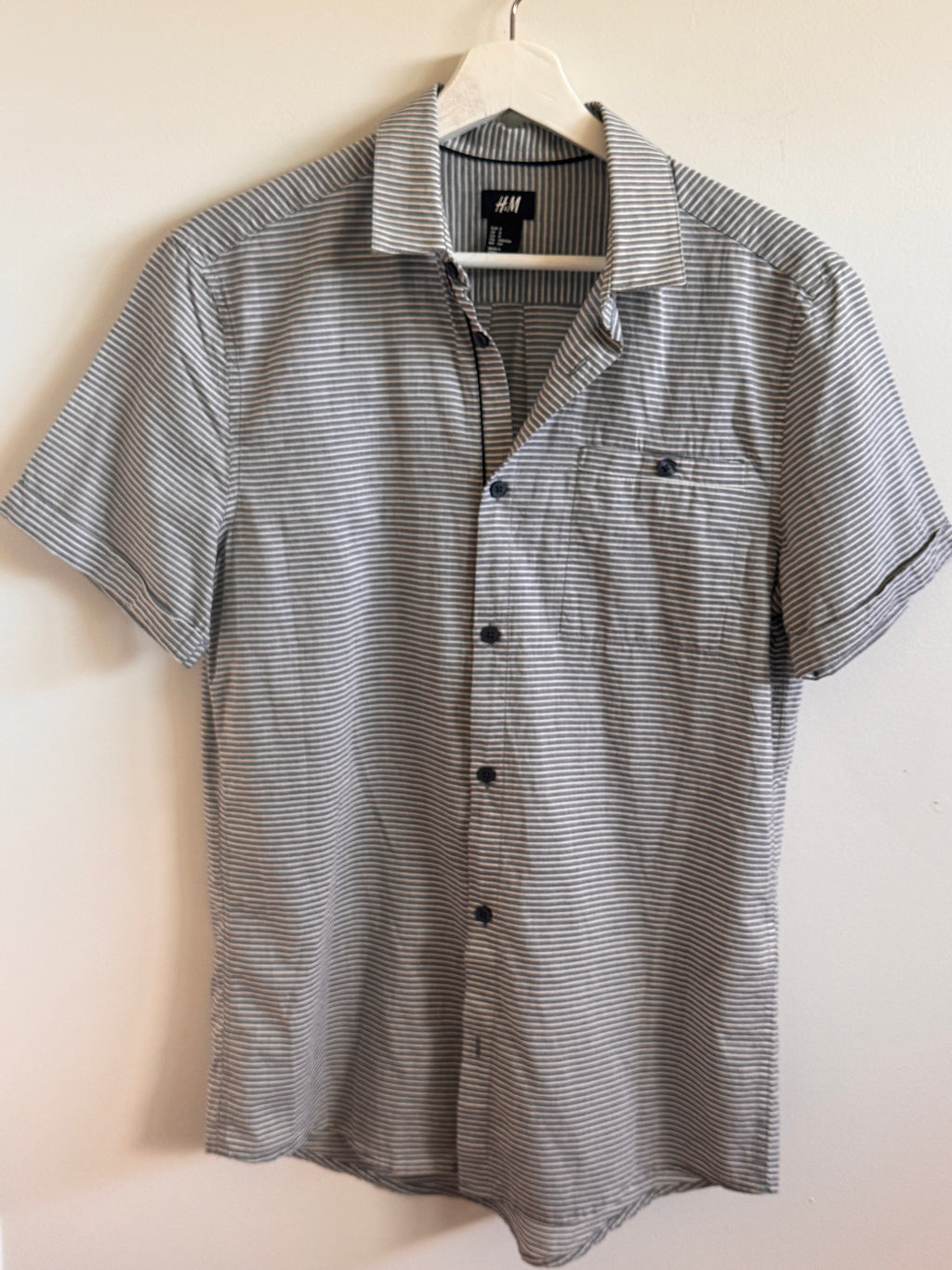Hanging gray striped shirt on a light beige surface