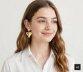 Woman wearing gold heart-shaped earrings against a plain background