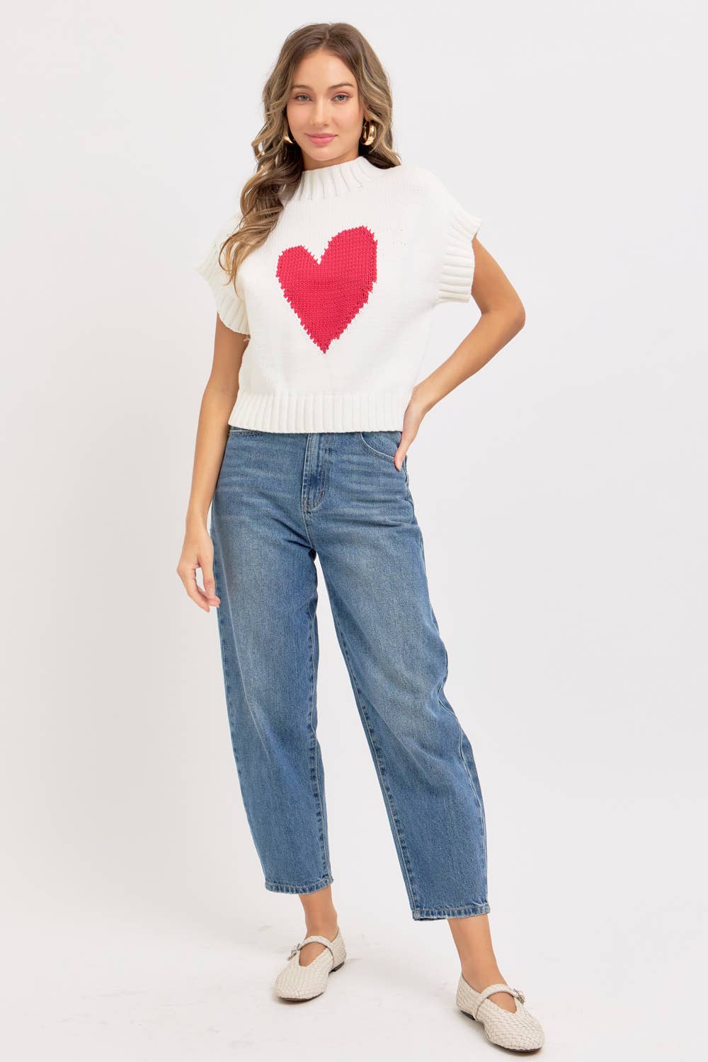 Woman wearing a white sweater with a red heart design and blue jeans on a white background