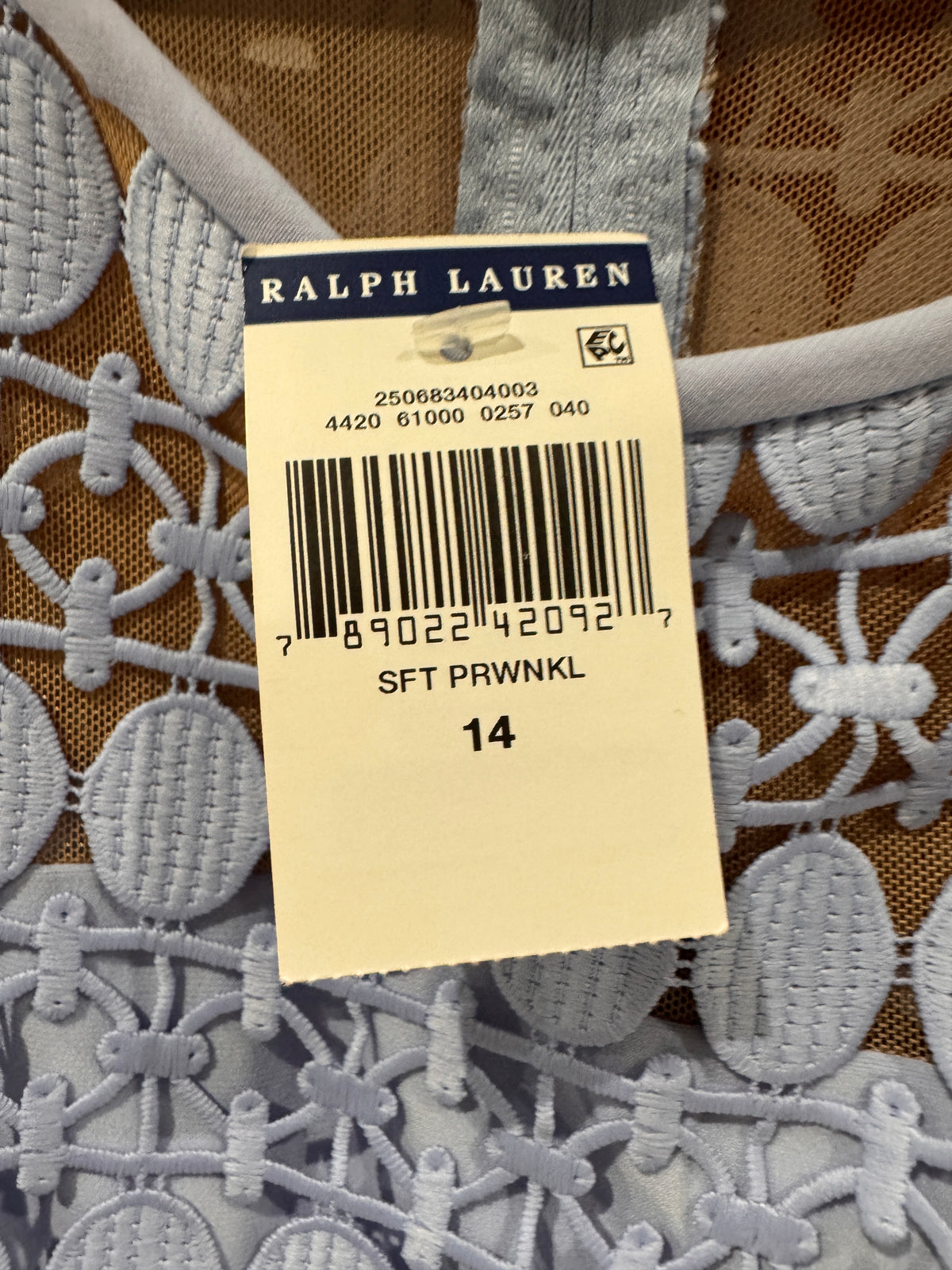 A close-up of a Ralph Lauren garment tag attached to a light blue-gray embroidered lace top. The tag shows the Ralph Lauren brand name, a barcode, and the size code SFT PRWNKL 14.