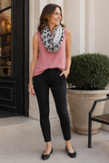 Woman wearing a pink sleeveless top and black pants with a patterned scarf outdoors.