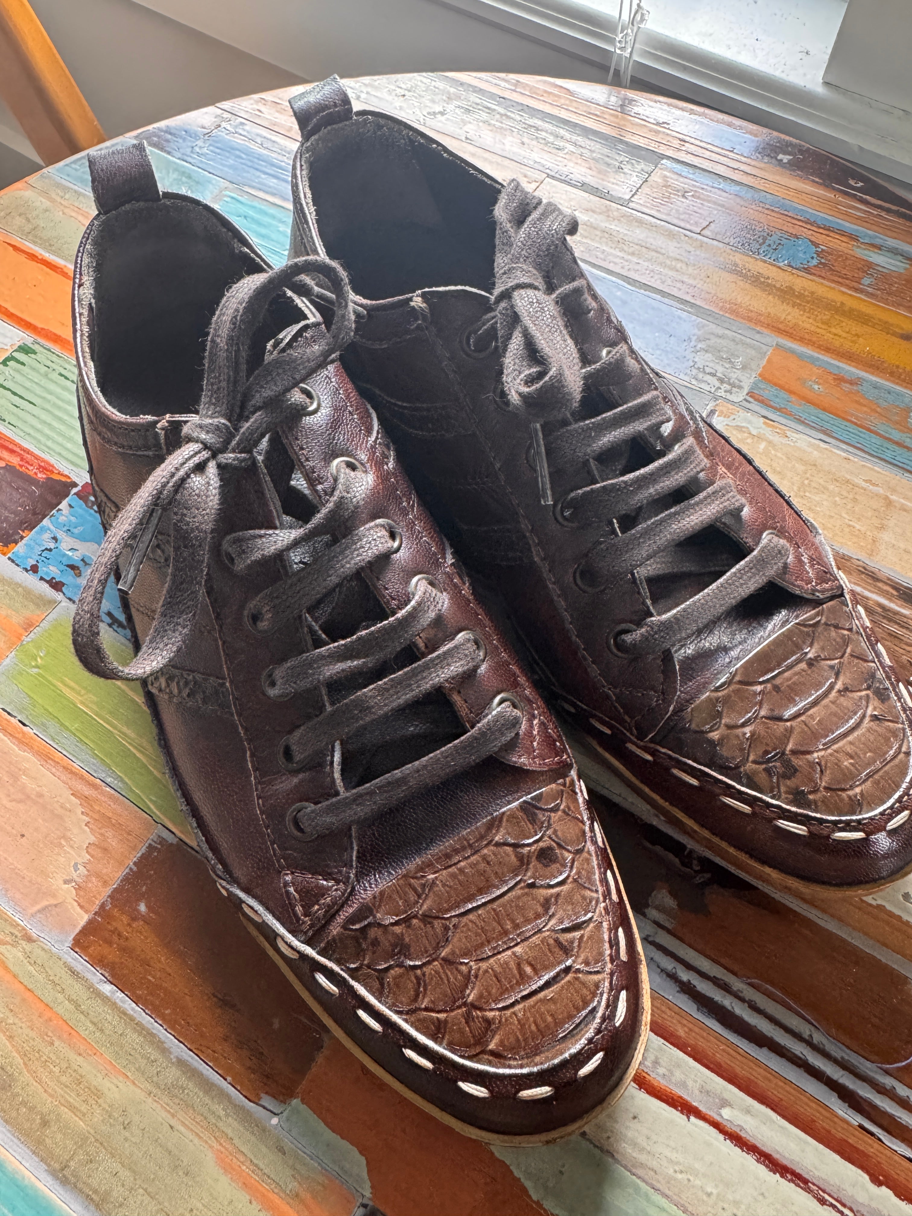 Pair of brown leather shoes with textured sole on a colorful wooden surface