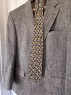 A men's gray textured herringbone blazer jacket displayed on a hanger with a patterned necktie and pocket square.