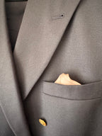 Close-up of a dark gray textured blazer jacket with a single gold button and a beige pocket square in the breast pocket.